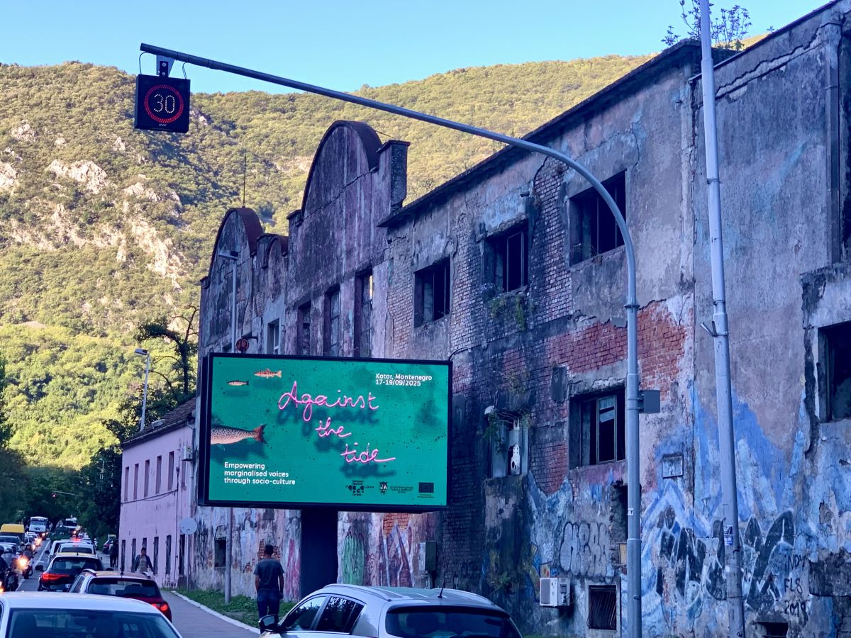 Plakat mit Ankündigung der ENCC Konferenz "Against the Tide" vor einem verfallenen Fabriksgebäude – September 2025, Kotor / Montenegro,